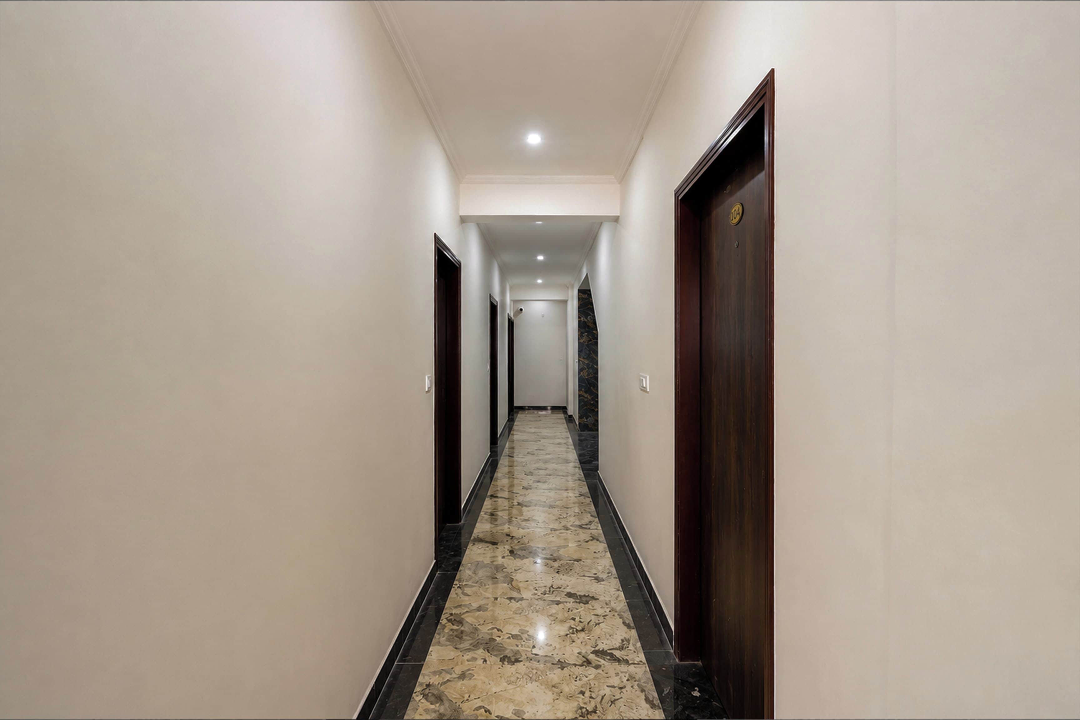 Un pasillo de hotel con piso de mármol, puertas de madera y pared de color claro.