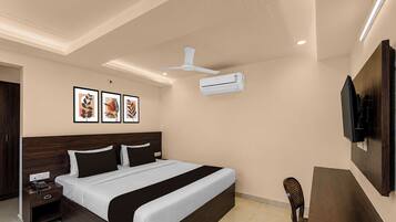 Habitación de hotel con cama, mesita de noche, ventilador de techo, televisor montado en la pared, equipo de aire acondicionado y obras de arte.