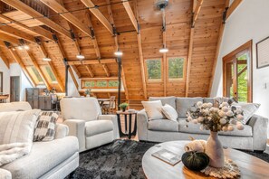 Un vaste espace de vie de style loft, doté de hauts plafonds, de poutres apparentes et de grandes fenêtres offrant une vue sur l’extérieur.