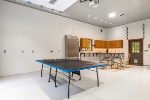 A spacious room with a ping pong table, a kitchenette, and a door leading outside.