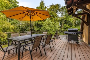 Une terrasse extérieure avec une table et des chaises, un barbecue et un grand parasol.