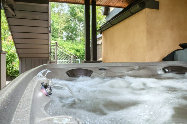 A hot tub with multiple jets, a wooden deck, and a view of a house and trees.