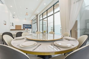 Een moderne eetruimte met een ronde tafel, witte stoelen en een groot raam met gordijnen.