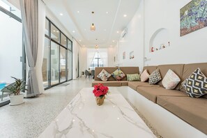 A modern living room with a marble coffee table, a sofa with patterned cushions, and a large window with curtains. - Villa C | 6BR Private Pool | Central Pattaya (Pattaya City)