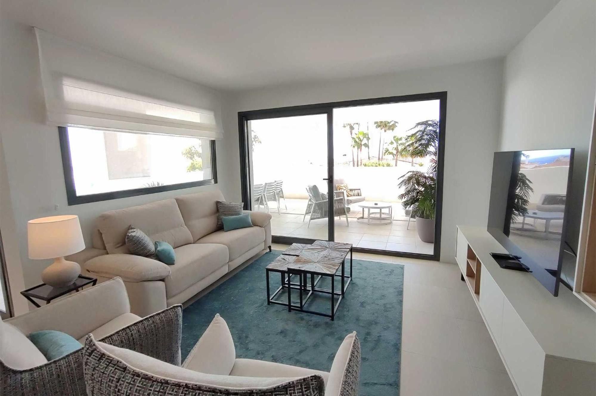 A modern living room with a sofa, armchairs, a coffee table, a TV, and a sliding glass door leading to an outdoor patio.