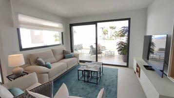 A modern living room with a sofa, armchairs, a coffee table, a TV, and a sliding glass door leading to an outdoor patio.
