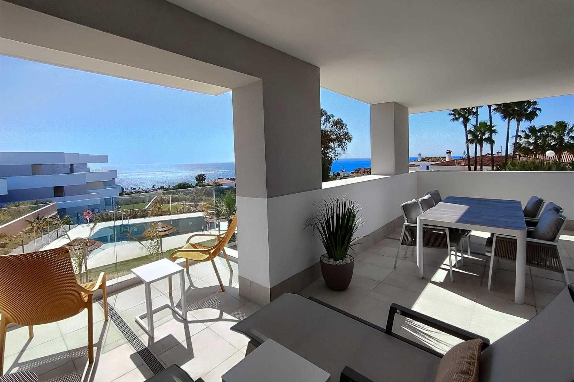 Un balcón con mesa y sillas, una planta en maceta y vistas al mar y edificios.