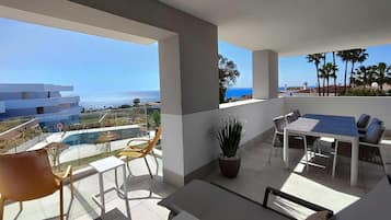 Un balcón con mesa y sillas, una planta en maceta y vistas al mar y edificios.