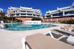 A swimming pool with lounge chairs and a building with multiple balconies in the background. - Apartment 'Pure South' with Mediterranean Views (Manilva)