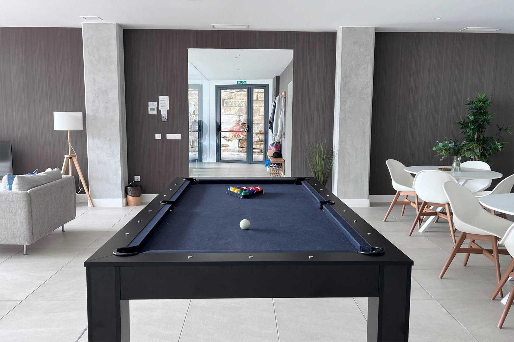Een pooltafel met ballen, een bank, een lamp en een eethoek met stoelen en een tafel.