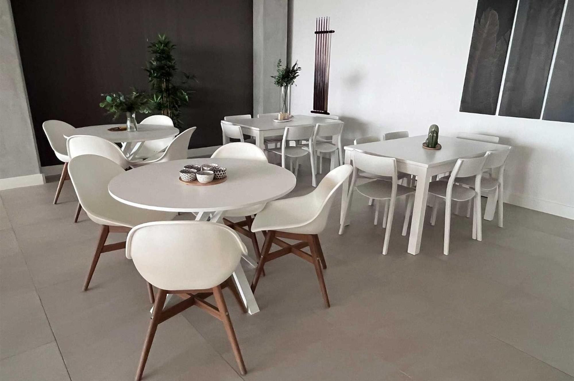 Un espace repas moderne avec des tables rondes et des chaises blanches, caractérisé par un design minimaliste et une palette de couleurs neutres.