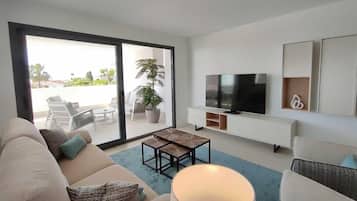 A modern living room with a sofa, a coffee table, a TV, and a sliding glass door leading to an outdoor seating area.
