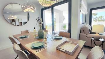 Un comedor con una mesa de madera, sillas y un jarrón con flores. Hay botellas de vino y copas sobre la mesa.