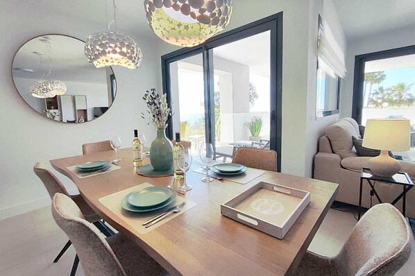 A dining area with a wooden table, chairs, and a vase with flowers. There are wine bottles and glasses on the table. - Apartment 'Pure South' with Mediterranean Views (Manilva)