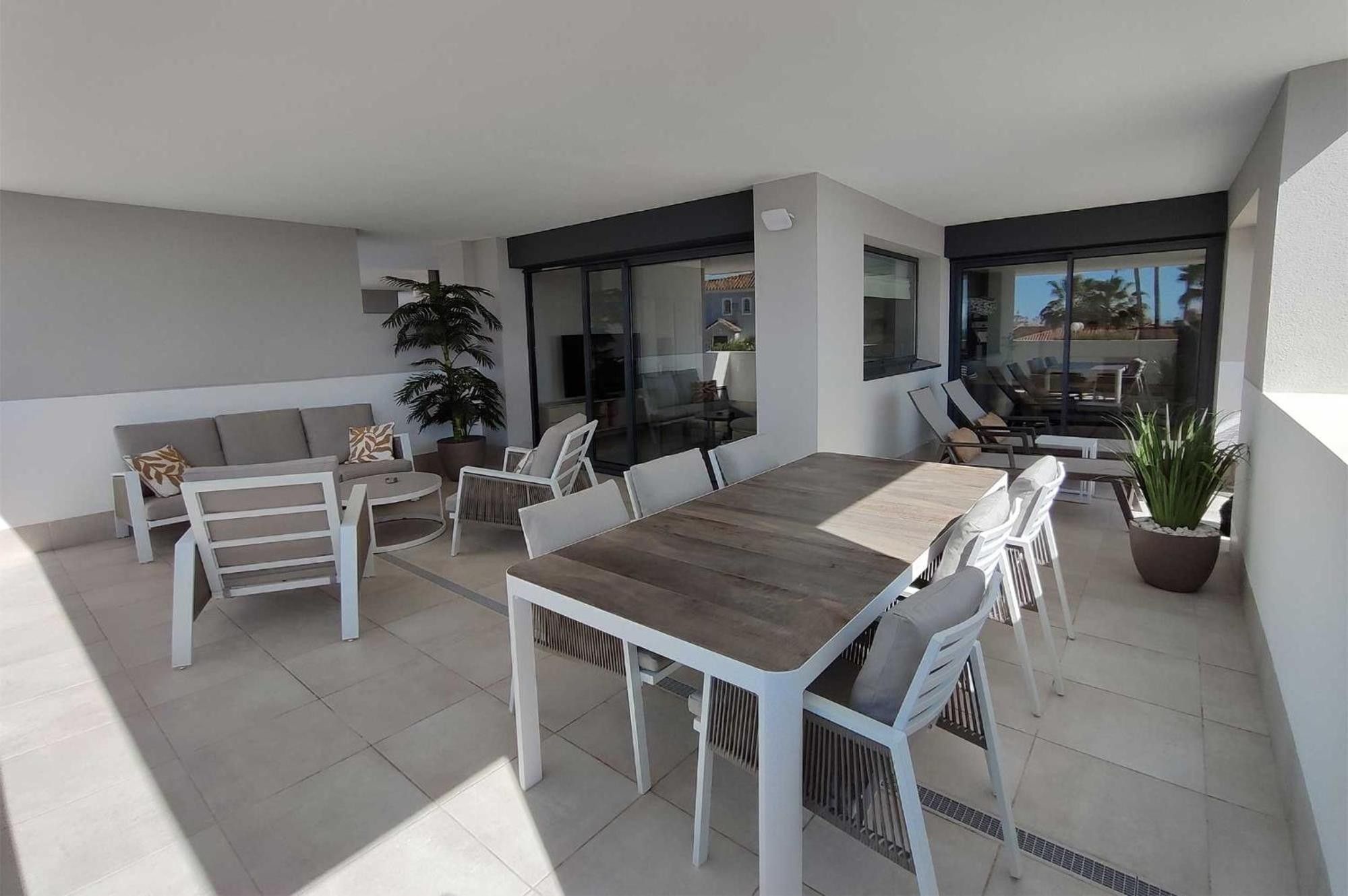 A modern outdoor patio with a dining table, chairs, a sofa, and potted plants.