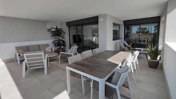 A modern outdoor patio with a dining table, chairs, a sofa, and potted plants.