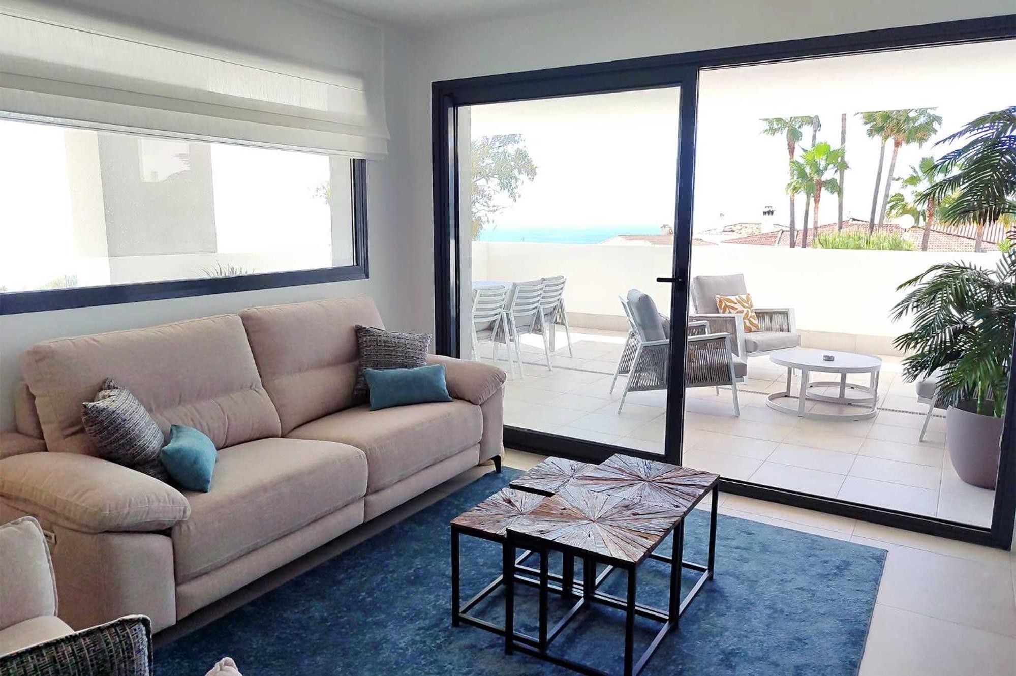 Una sala de estar con un sofá, una mesa de centro y vistas a un patio exterior con sillas y una mesa.