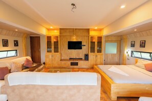 Een ruime slaapkamer met een groot bed, een kleinere bank en een televisie bevestigd aan een houten wandpaneel.