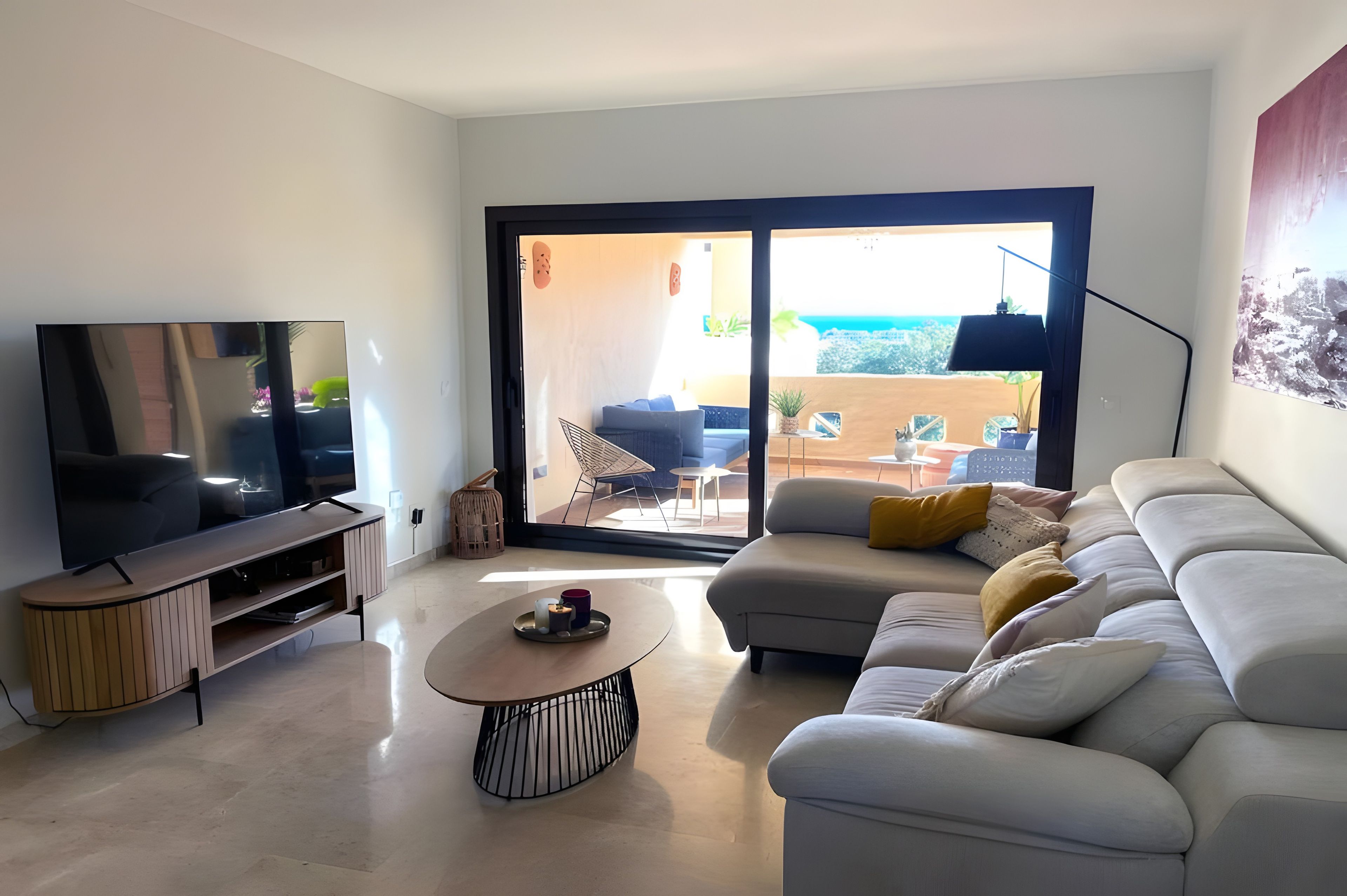 Een moderne woonkamer met een flatscreen televisie, een bank, een bijzettafeltje en een schuifpui naar een terras.