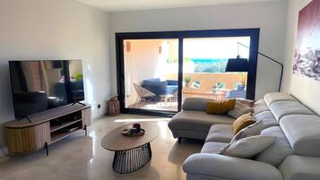 Een moderne woonkamer met een flatscreen televisie, een bank, een bijzettafeltje en een schuifpui naar een terras.