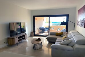 Een moderne woonkamer met een flatscreen televisie, een bank, een salontafel en uitzicht op een terras.