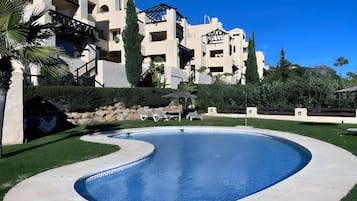Una piscina de borde curvo, rodeada por un césped cuidado y un edificio con varios balcones.