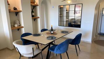 A dining area with a table set for four, blue and white chairs, a wine bottle, and a decorative mirror.