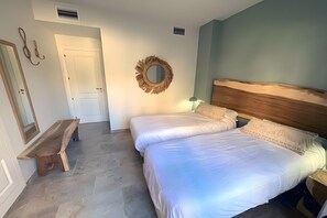 Un dormitorio con dos camas, un banco de madera, un espejo y una corona decorativa en la pared.