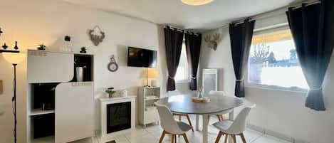 A modern living room with a dining table, chairs, a TV, and a fireplace.