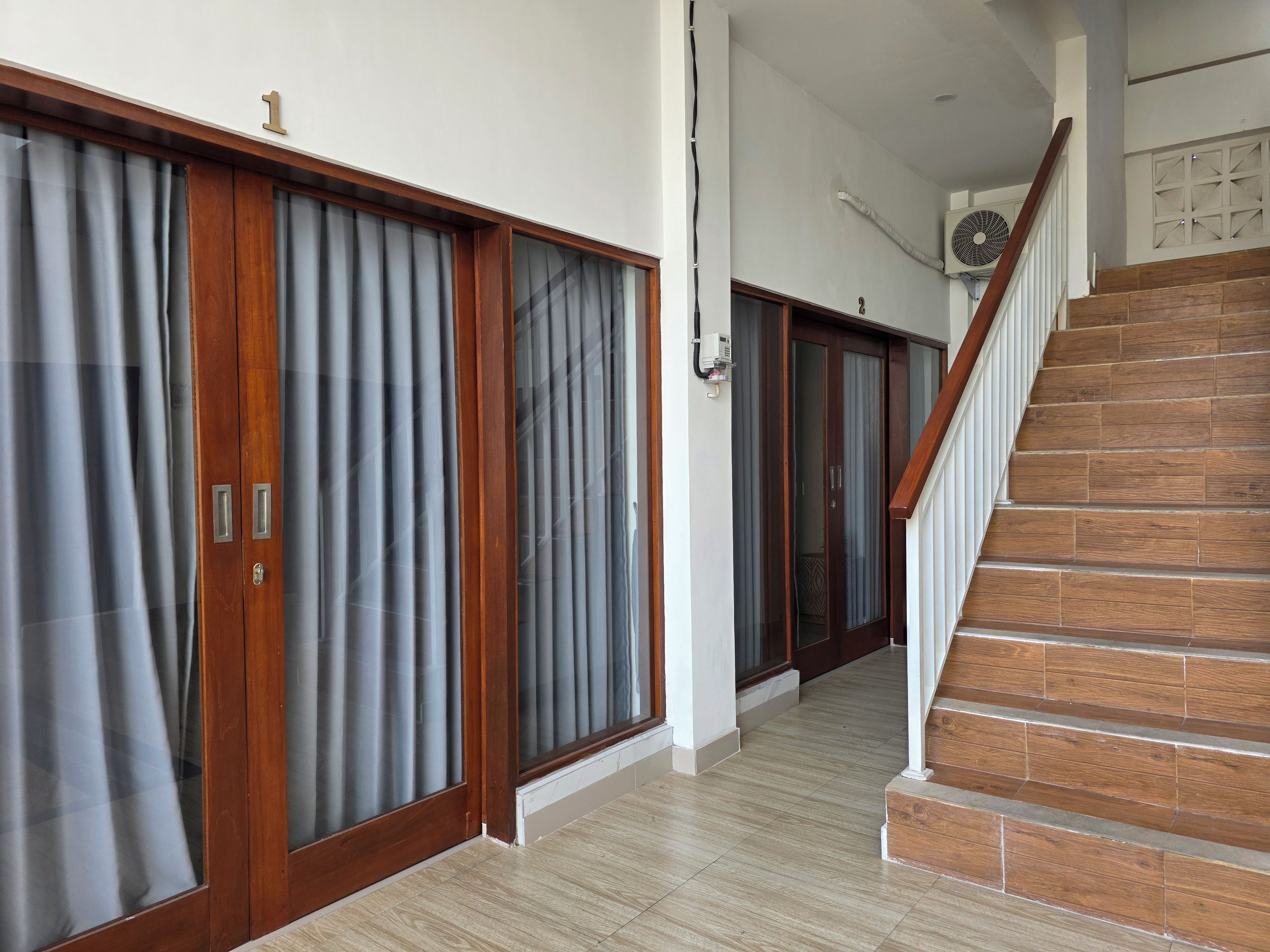 Un pasillo con una escalera de madera, una puerta con el número 1 y un equipo de aire acondicionado instalado en la pared.