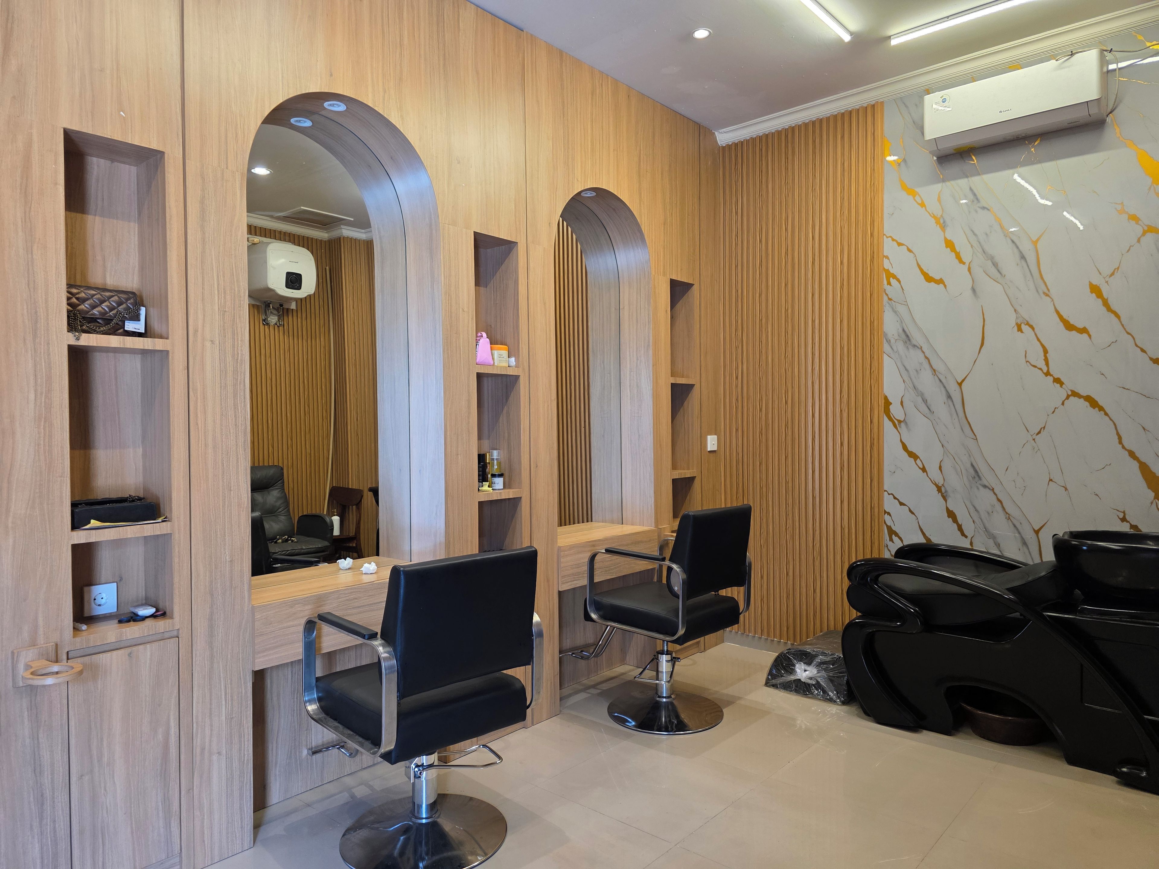 Un salón con dos sillas de peluquería negras, paneles de madera y una pared con estampado de mármol.