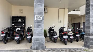 Een bord van een motorscooterverhuur, meerdere scooters geparkeerd in een overdekte ruimte, en de ingang van een gebouw.