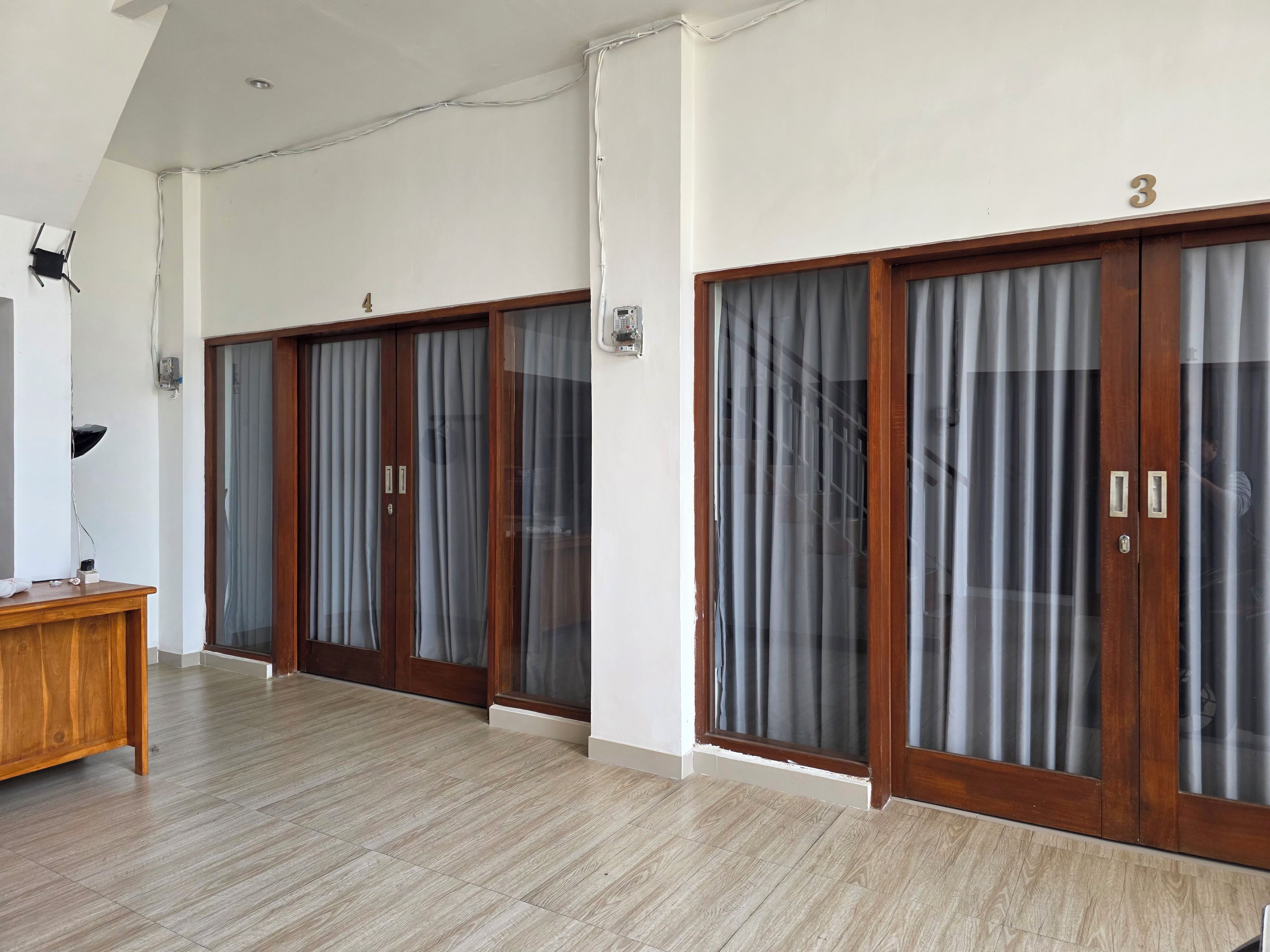 Habitación de hotel con piso de madera, un escritorio y dos grandes puertas correderas con cortinas.