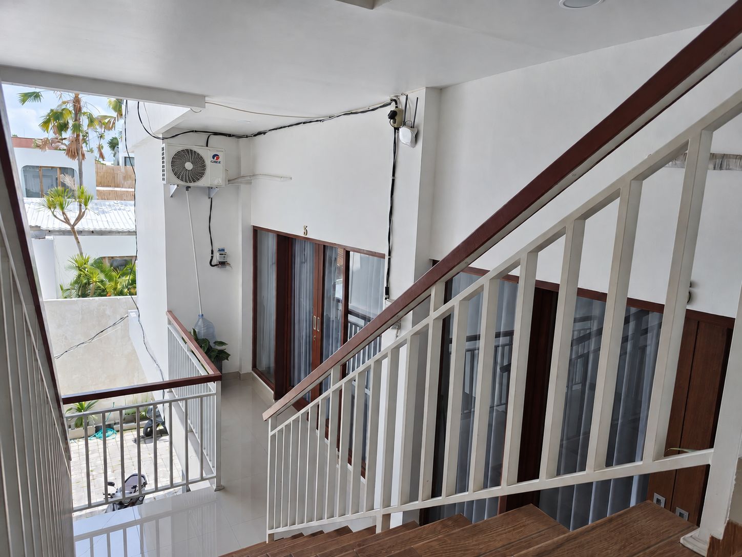 Ein Wohnbalkon mit Holzgeländer, einem Deckenventilator und Blick auf ein Nachbargebäude.