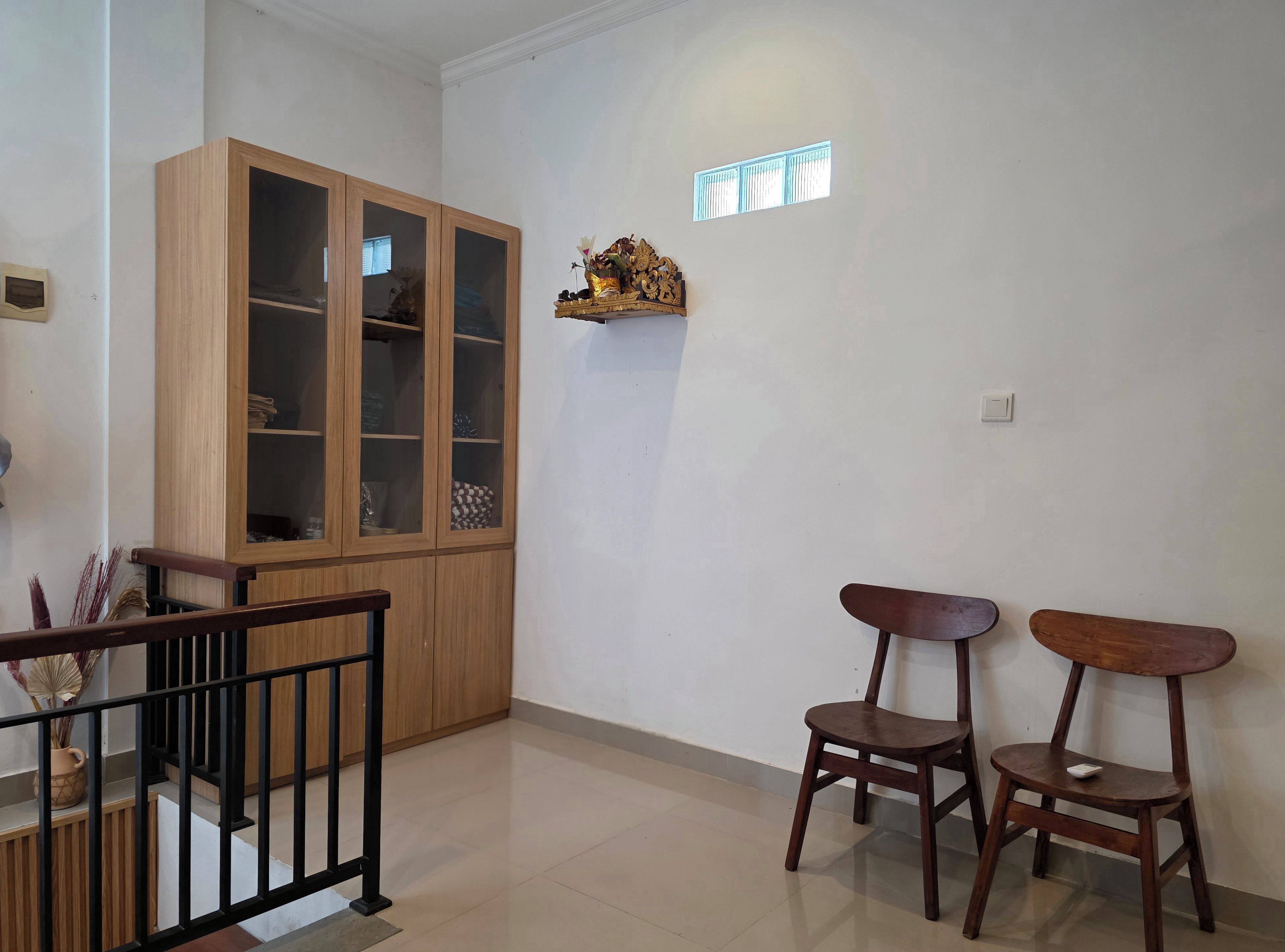 A room with a wooden cabinet, two chairs, a small table, and a decorative piece on the wall.