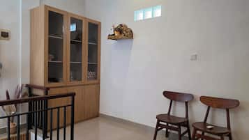 A room with a wooden cabinet, two chairs, a small table, and a decorative piece on the wall.