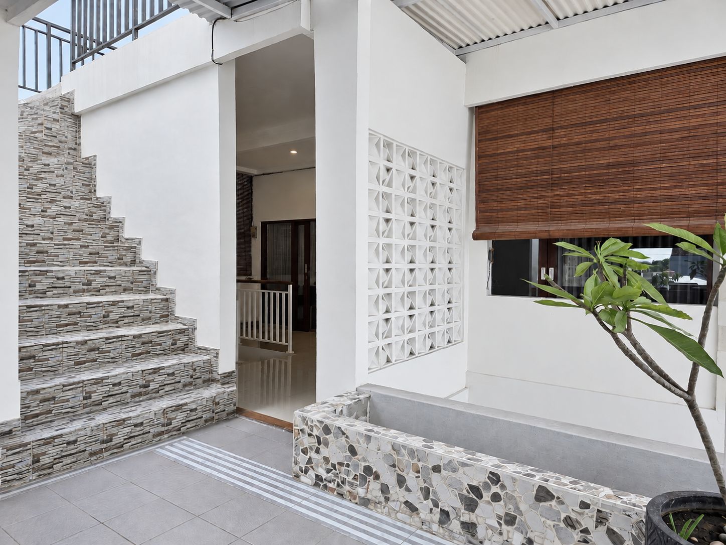 Una casa moderna con una escalera de piedra, una pared blanca con un diseño geométrico y un persiano de madera.