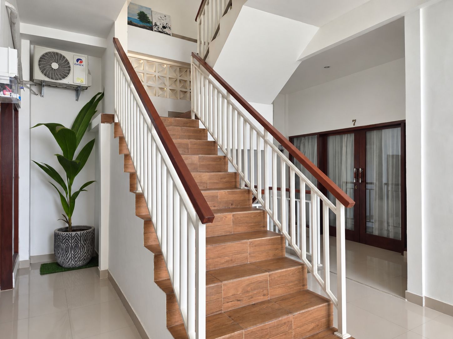 Una escalera con escalones de madera y barandillas blancas, que lleva a un rellano con un panel decorativo en la pared y un ventilador de techo.
