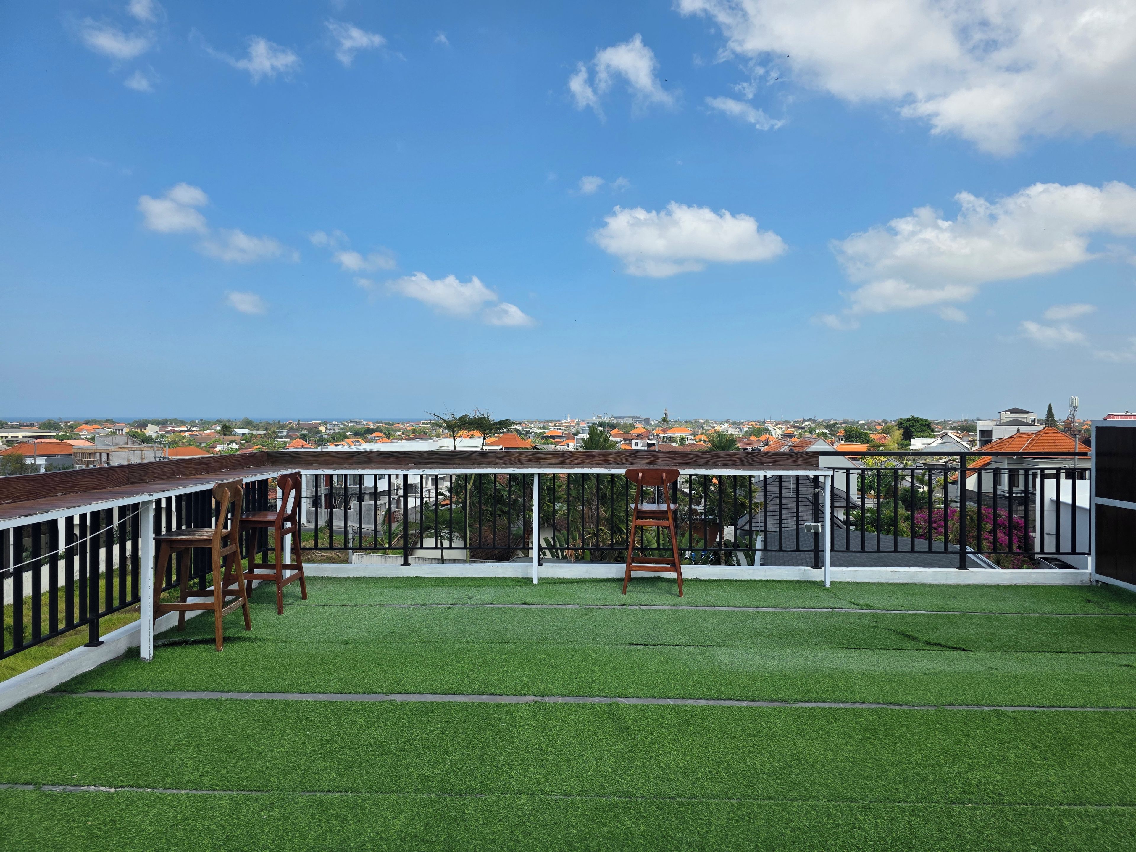 Una terraza en la azotea con césped artificial, barandilla y dos sillas de madera.