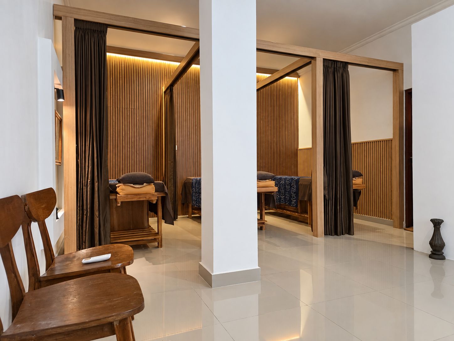 Habitación de hotel con una silla de madera, una mesita pequeña, una cama con colcha estampada y un ventanal grande con cortinas.
