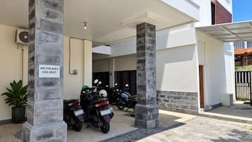 A covered parking area with motorbikes for rent, a potted plant, and a sign indicating the availability of motorbikes for rent.