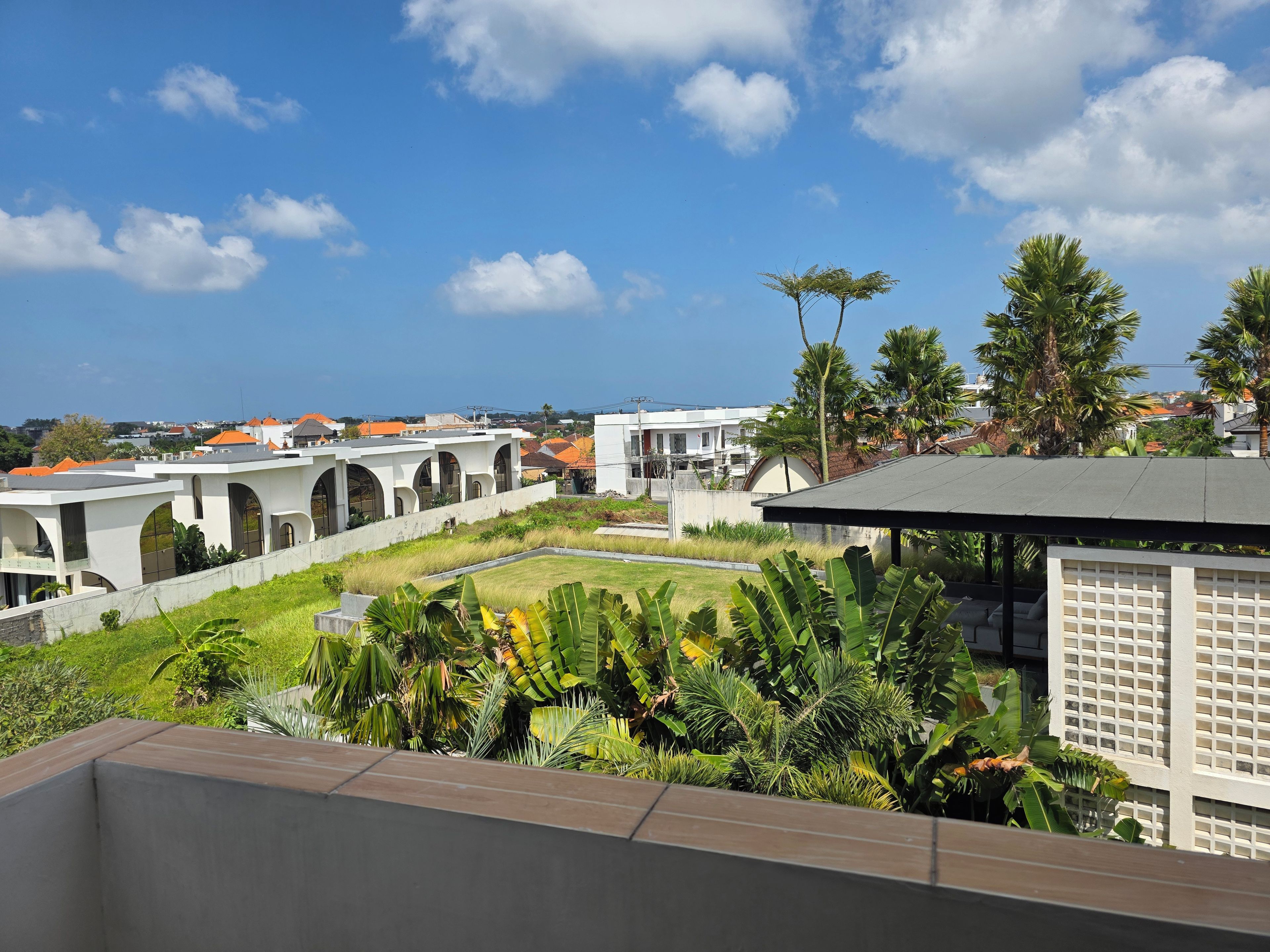 A residential area with white buildings, a grassy courtyard, and tropical vegetation.