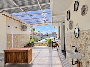 A covered outdoor area with a wooden table, chairs, a sink, and decorative plates on the wall.