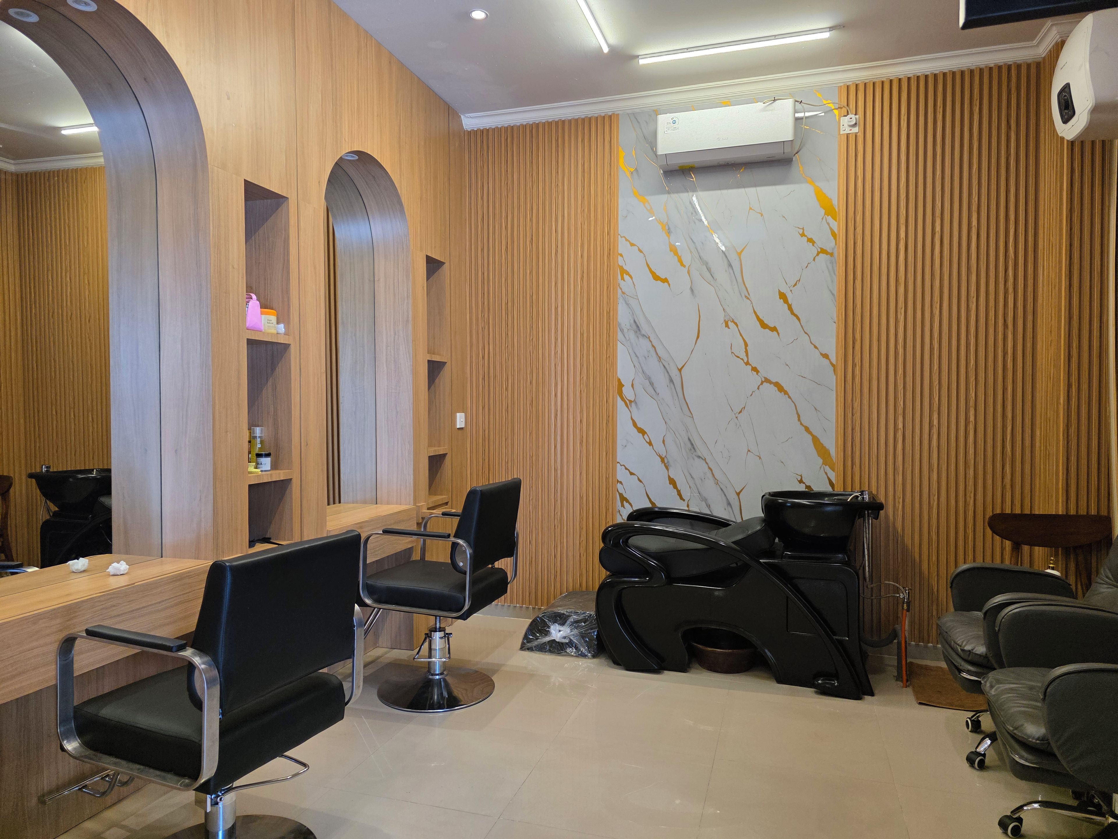 Un salón con un mostrador de recepción de madera, varias sillas de peluquería negras y una pared con diseño de mármol.