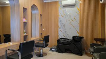 Een kapsalon met een houten receptiebalie, meerdere zwarte kappersstoelen en een wand met een marmerlook.