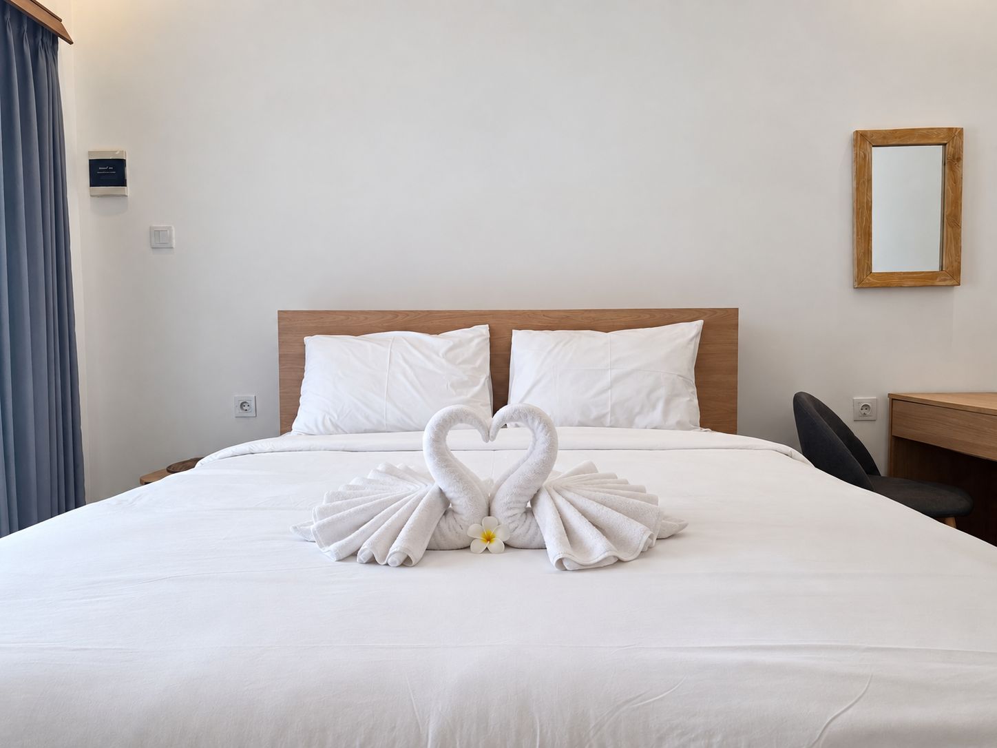 Une chambre d’hôtel avec un lit, une tête de lit en bois, un bureau et un miroir.