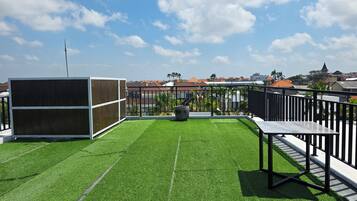 Una terraza en la azotea con césped artificial, una mesa de metal y una estructura de madera.