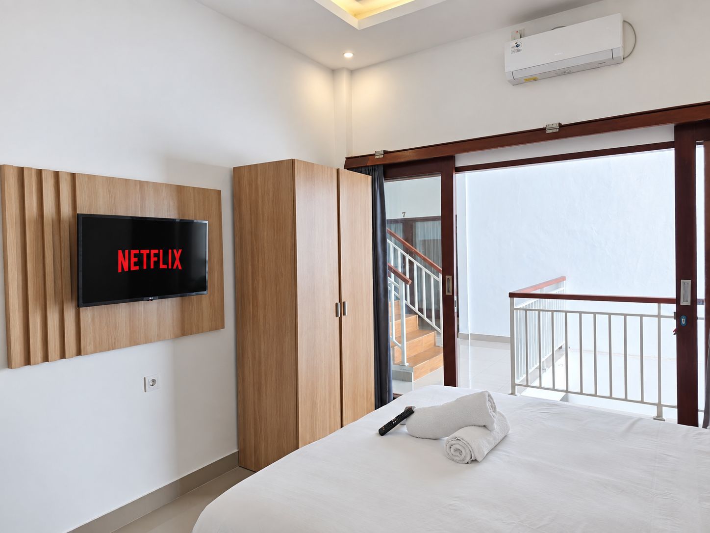 Habitació d'hotel amb llit, televisió penjada a la paret, balcó amb barana i aire condicionat.