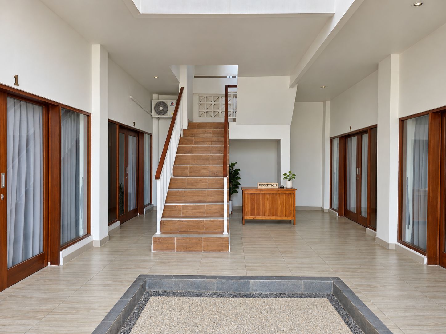 Un interior espacioso con una escalera central, mostrador de recepción de madera y puertas de cristal a ambos lados.