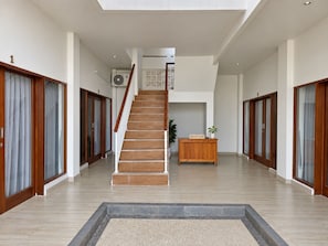 Un interior espacioso con una escalera central, mostrador de recepción de madera y puertas de cristal a ambos lados.